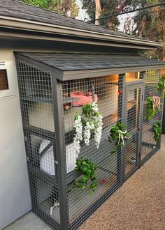 a small cage with flowers and plants in it on the side of a building next to a mailbox