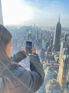 a woman taking a photo from the top of a building with her cell phone in new york city