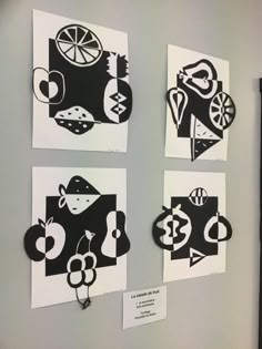 four pieces of paper cut into shapes on a gray wall with black and white artwork