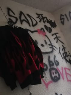 graffiti is spray painted on the wall next to a black and red jacket hanging from a hook