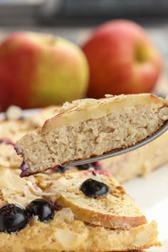 a piece of cake with blueberries and apples on the side is being held by a fork