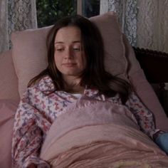 a woman laying in bed with her head on the pillow and looking at the camera