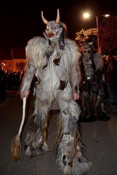 two men in costume walking down the street at night with long hair and horns on