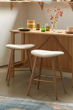 two stools in front of a wooden table with plates and bowls on top of it