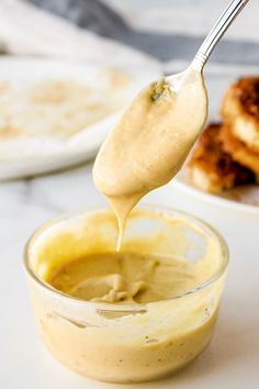 a spoon full of sauce being lifted from a glass bowl with pancakes in the background