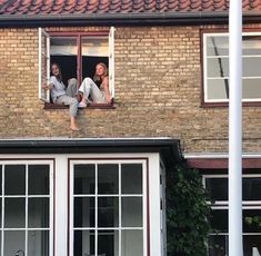 two women sitting in the window of a brick building