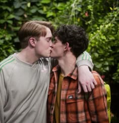 two young men kissing each other in front of trees