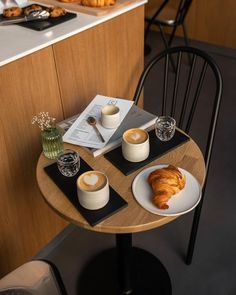 two plates with croissants and coffee are on a small table in front of the counter