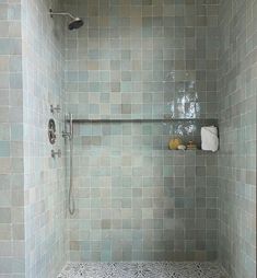 a tiled shower in a bathroom next to a shelf with soaps and other items