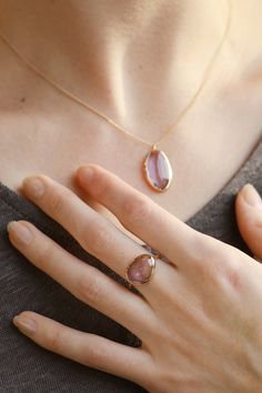 a woman's hand wearing a gold ring with a pink agate stone on it