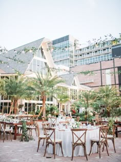 an outdoor dining area with tables, chairs and palm trees in front of a large building