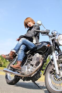 a woman sitting on top of a motorcycle in the middle of the road with her legs crossed