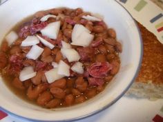 a white bowl filled with beans and onions on top of a table next to a piece of bread