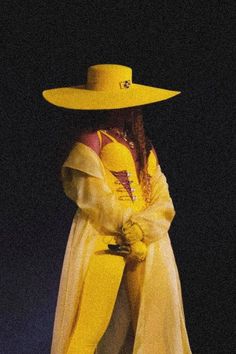 a woman wearing a yellow hat and dress with a long veil on her head, standing in front of a black background