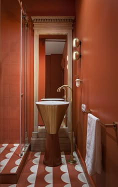 a bathroom with an orange wall and white polka dots on the floor, along with a gold pedestal sink