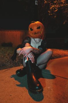 a woman sitting on the ground with her legs crossed wearing a pumpkin mask and boots