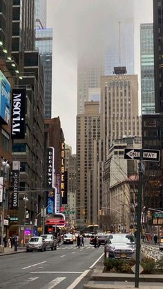 a city street filled with lots of traffic and tall buildings in the background, on a foggy day