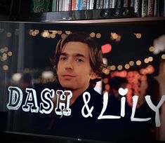 a television screen with the words dash and lily on it in front of a bookshelf