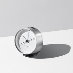 a silver clock sitting on top of a white table next to a gray and white wall