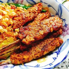 some meat and vegetables are on a blue and white plate with purple flowers around it