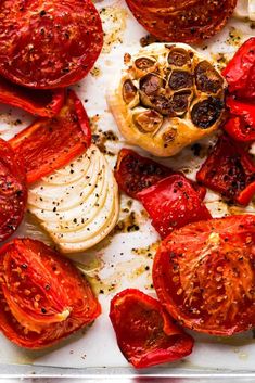 sliced tomatoes and onions on a baking sheet with seasoning sprinkled around them