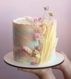 a hand holding a cake with flowers on it