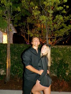 a man and woman standing next to each other in front of a tree at night