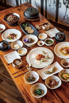 a wooden table topped with lots of plates and bowls filled with different types of food