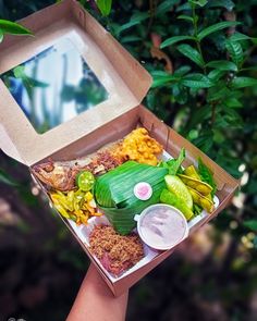 an open box filled with food sitting on top of a table next to a tree