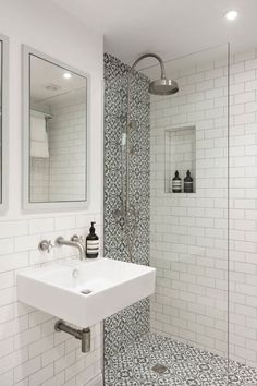 a white bathroom with black and white tile on the floor, shower stall and sink