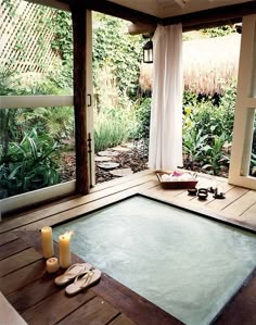 an indoor hot tub with candles and sandals on the floor next to it, surrounded by greenery