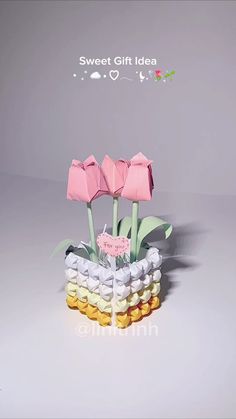 three pink flowers are in a vase filled with small marshmallows and candy