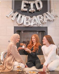 three women sitting on the floor in front of a sign that says eid lubaran