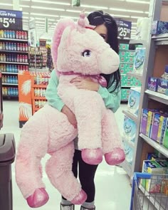 a woman is holding a large pink stuffed animal in a grocery store's aisle