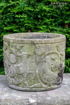 a stone planter sitting on top of a cement slab in front of some bushes