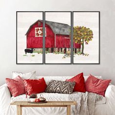 three red barn paintings hanging on the wall above a white couch with pillows and throw pillows