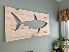 a wooden shark cut out on the wall next to a potted plant and window