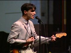 a man in a suit and tie holding a guitar while standing next to a microphone