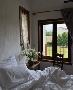 an unmade bed with white sheets and pillows in front of a large open window