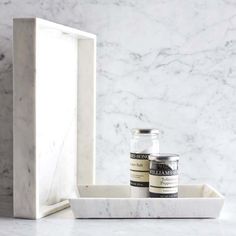 two jars sitting on top of a marble counter next to a white box with black writing