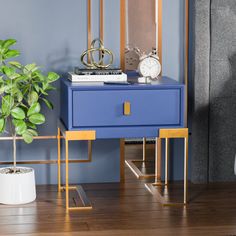 a blue and gold side table with a clock on it next to a potted plant