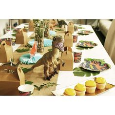 an image of a dinosaur party setting with cupcakes and desserts on the table