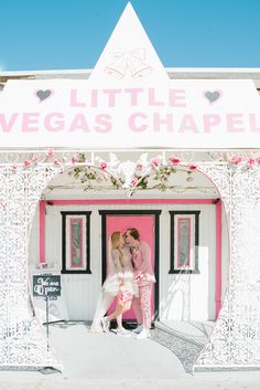 two brides kissing in front of a pink and white building with the words little vegas chapel painted on it