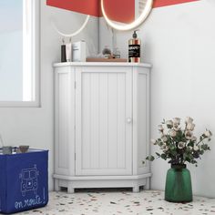 a white cabinet sitting next to a vase with flowers in it and a mirror on the wall