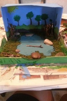 a paper model of a pond with rocks and grass in the middle, sitting on top of a table