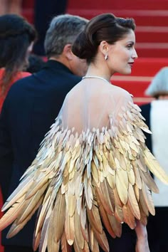 the back of a woman's dress with large feathers on it and people in the background