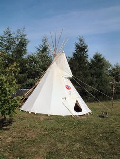 a teepee sitting on top of a lush green field next to trees and bushes