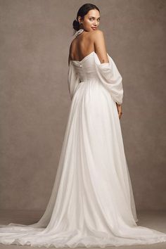 a woman in a white wedding dress with her back turned to the camera, posing