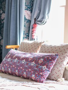 a bed with two pillows on top of it next to a window covered in curtains