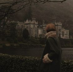 a woman standing in front of a large building on top of a lush green hillside